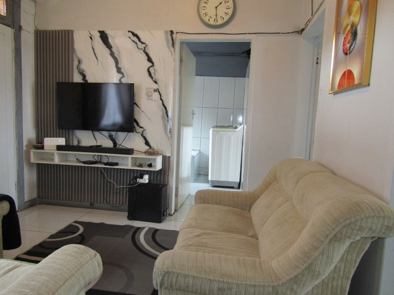 Living room featuring tiled flooring and a decorative feature wall with a built-in media shelf, providing access to an adjacent laundry area.