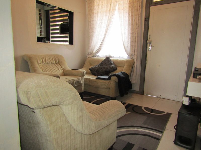 A compact living room featuring tiled flooring and an internal window, providing a functional space with potential for cosmetic updates.