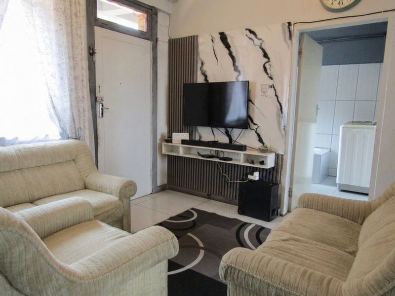 A living room featuring tiled flooring and a decorative feature wall with a built-in media shelf, providing access to adjacent rooms.