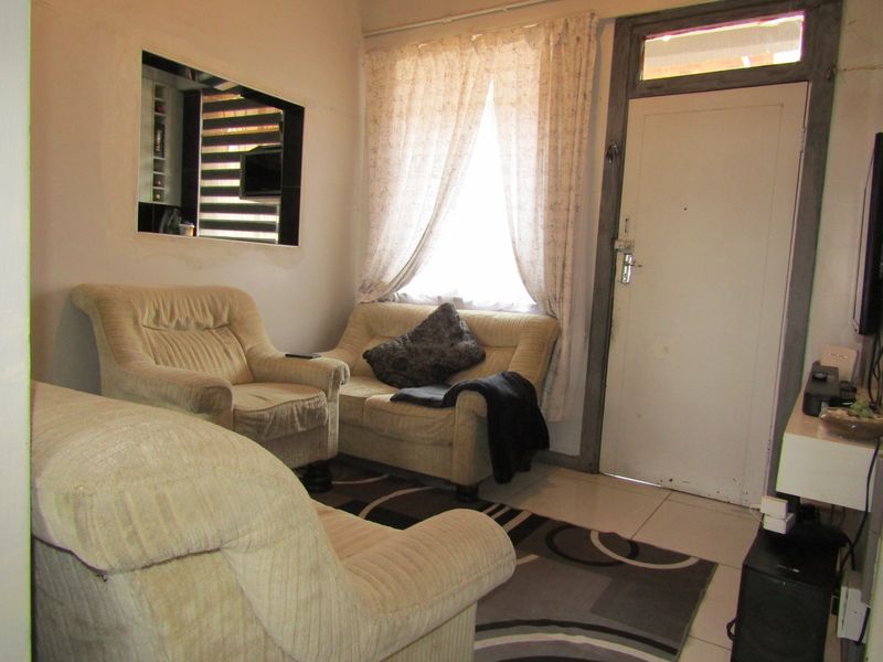 A compact living room featuring tiled flooring, an internal window, and a direct entrance door, offering a functional space with potential for cosmetic updates.