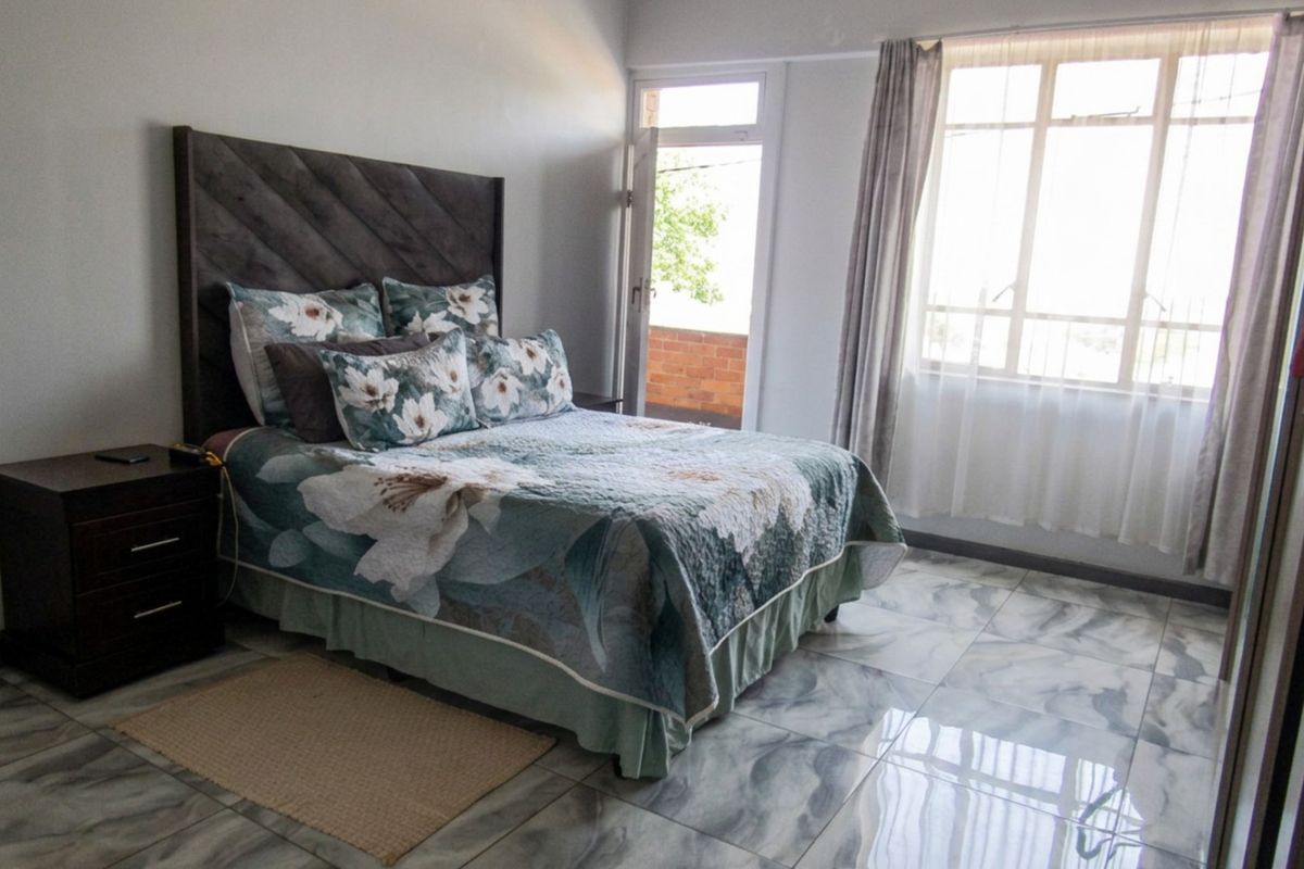 A well-lit bedroom featuring polished marble-effect floor tiles, a large window, and direct access to an outdoor balcony area.