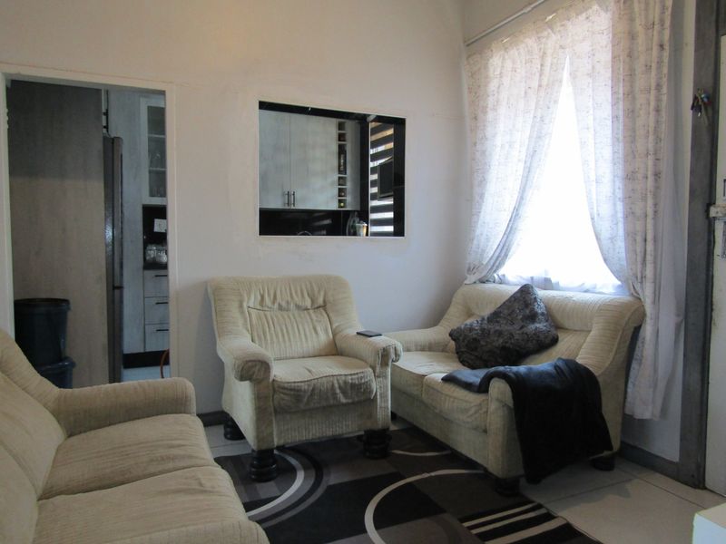 A living room featuring tiled flooring and a pass-through window connecting to the kitchen area, providing a functional layout for the apartment.