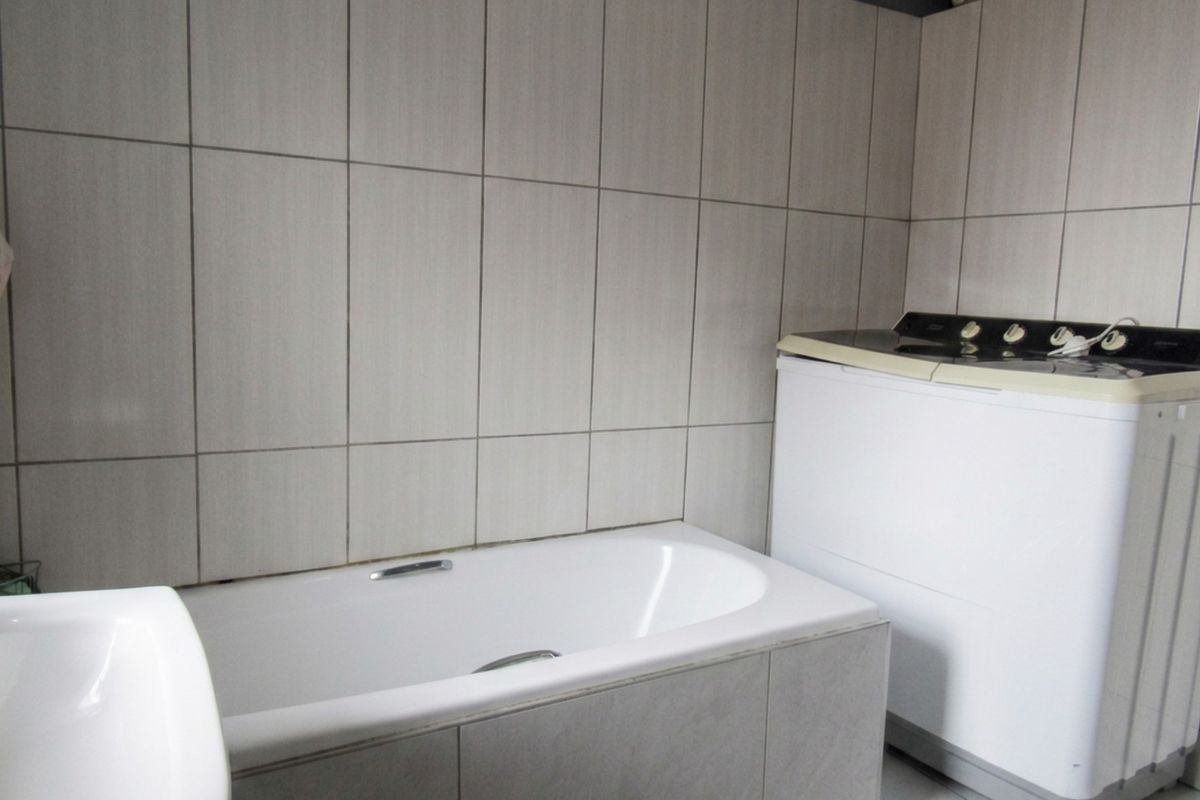 A functional bathroom featuring a built-in bathtub with neutral wall tiling and tiled flooring, providing a practical space for daily use.