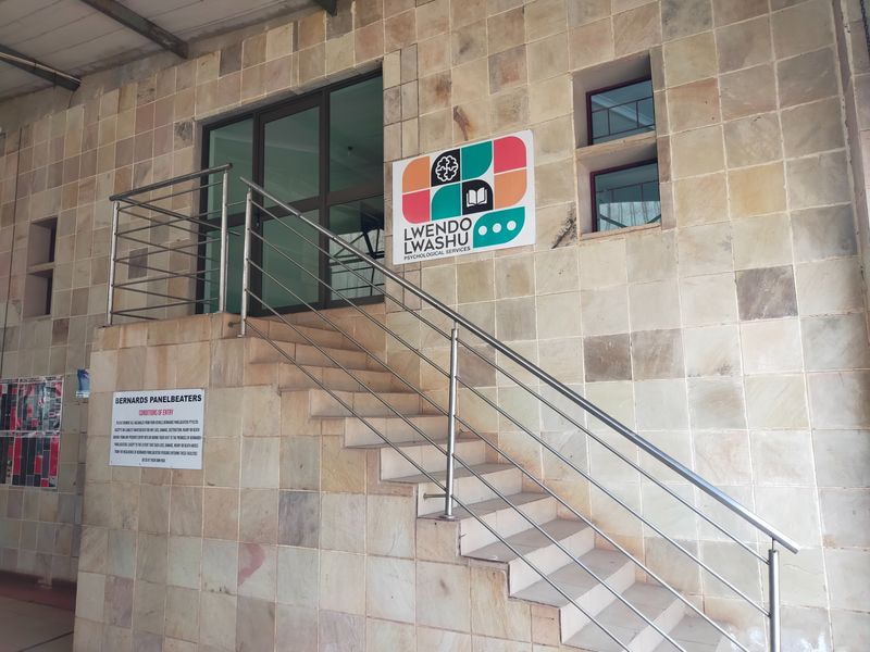 Front entrance of the office building featuring stone tile cladding, a concrete staircase with stainless steel handrails, and a glass door entry.