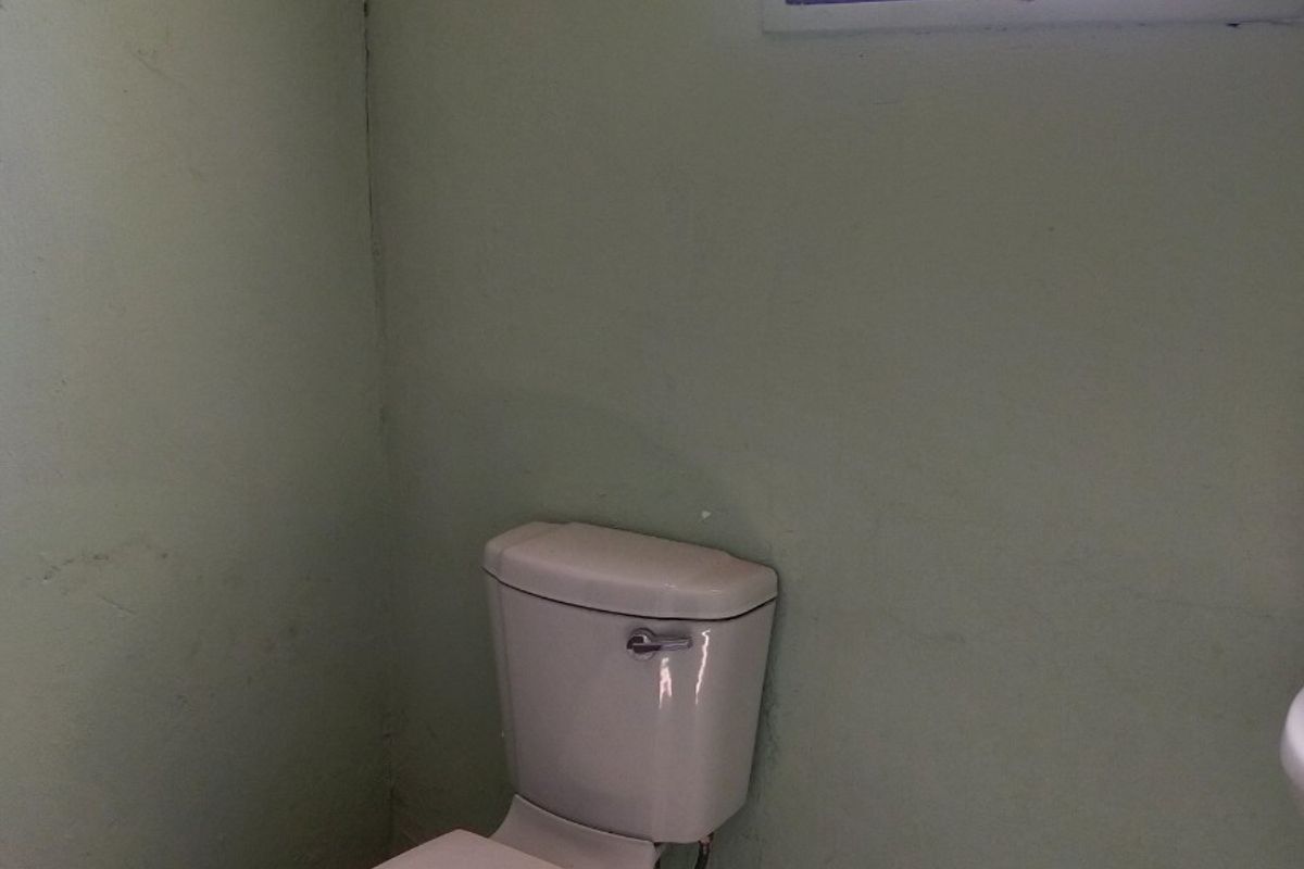 A small bathroom featuring a standard toilet, tiled flooring, and a window with security bars. The space requires maintenance and cosmetic updates.