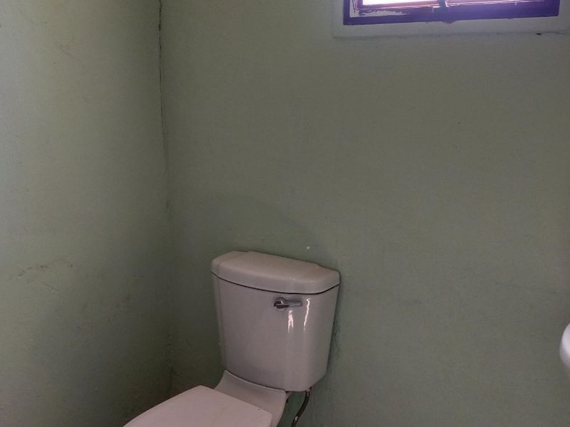 A small bathroom featuring a standard toilet, tiled flooring, and a window with security bars. The space requires maintenance and cosmetic updates.