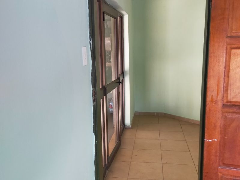 A vacant hallway featuring tiled flooring, a wooden door, and a sliding glass door leading to an adjacent space.