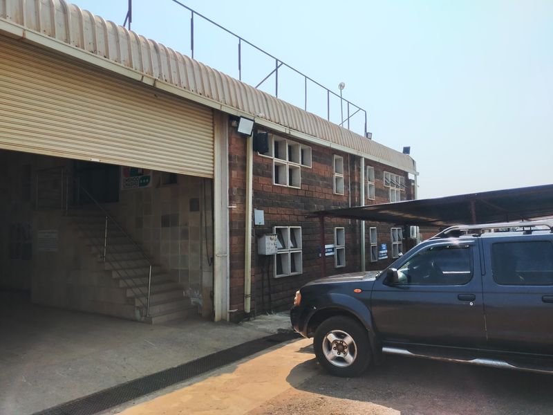 Exterior view of an office building featuring a large roller shutter door, brick facade, and an attached carport area.
