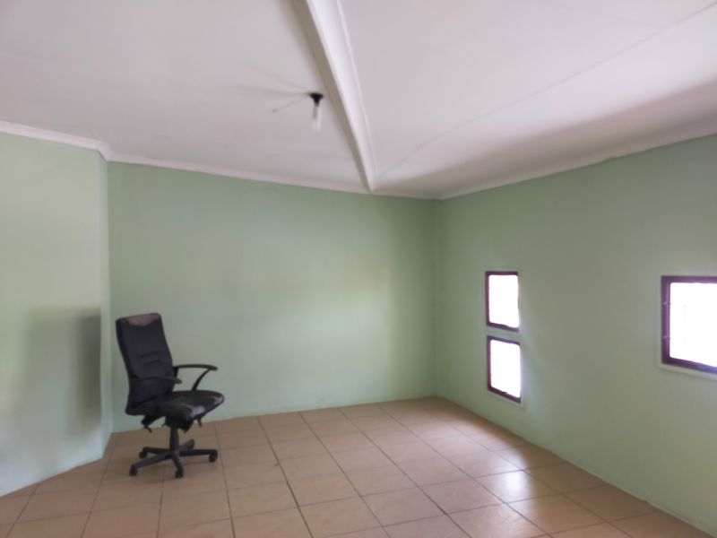A simple, vacant office space featuring tiled flooring, a vaulted ceiling, and small windows providing natural light.