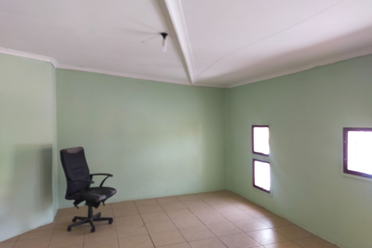 A simple, vacant office space featuring tiled flooring, a vaulted ceiling, and small windows providing natural light.