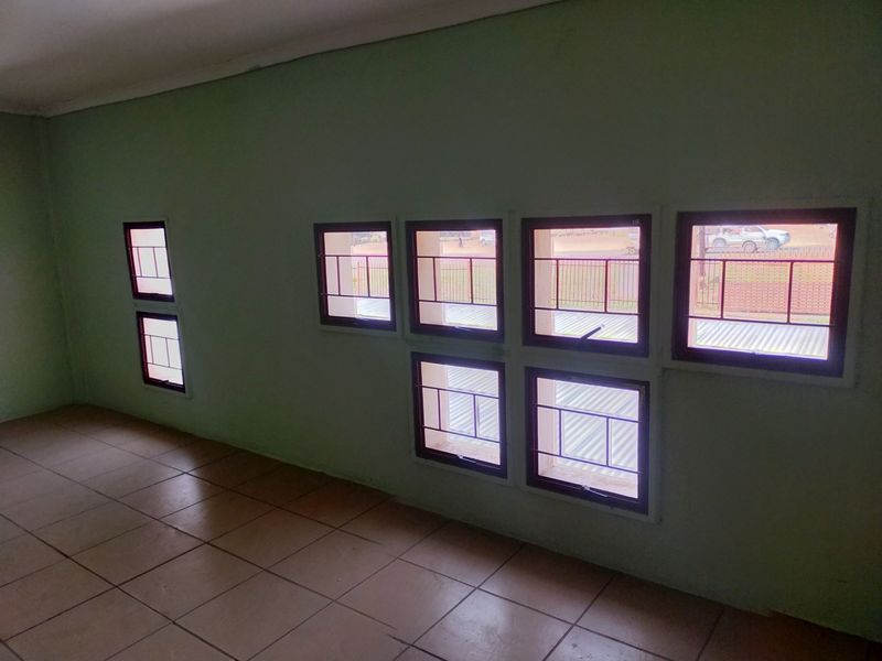 An empty office space featuring tiled flooring and multiple windows fitted with security bars, providing natural light and street views.