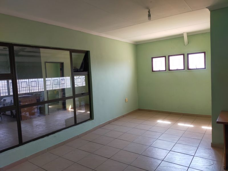 A vacant office space featuring tiled flooring, a large glass partition wall, and natural light from multiple windows.