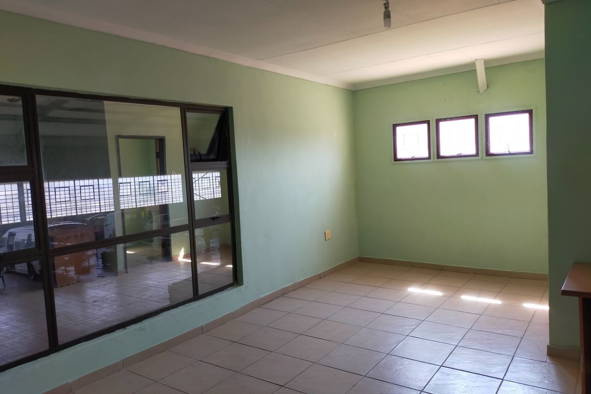 A vacant office space featuring tiled flooring, a large glass partition wall, and natural light from multiple windows.