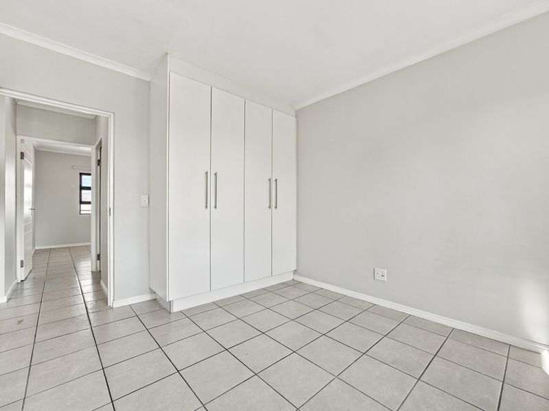 A bright, empty bedroom featuring neutral tiled flooring, white walls, and built-in cupboards, offering a clean and versatile space.