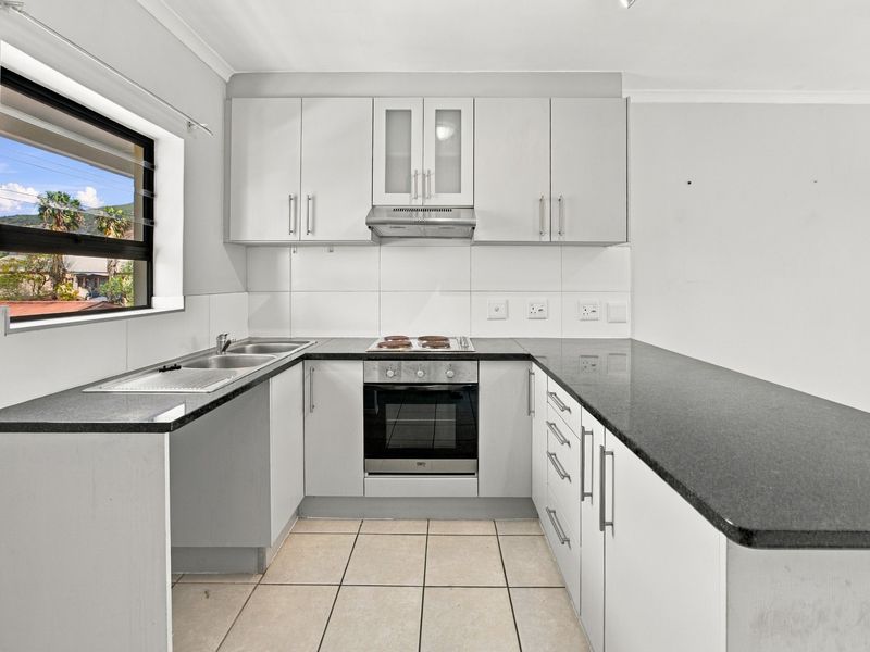 A functional U-shaped kitchen featuring white cabinetry, dark granite countertops, integrated oven and hob, and tiled flooring.