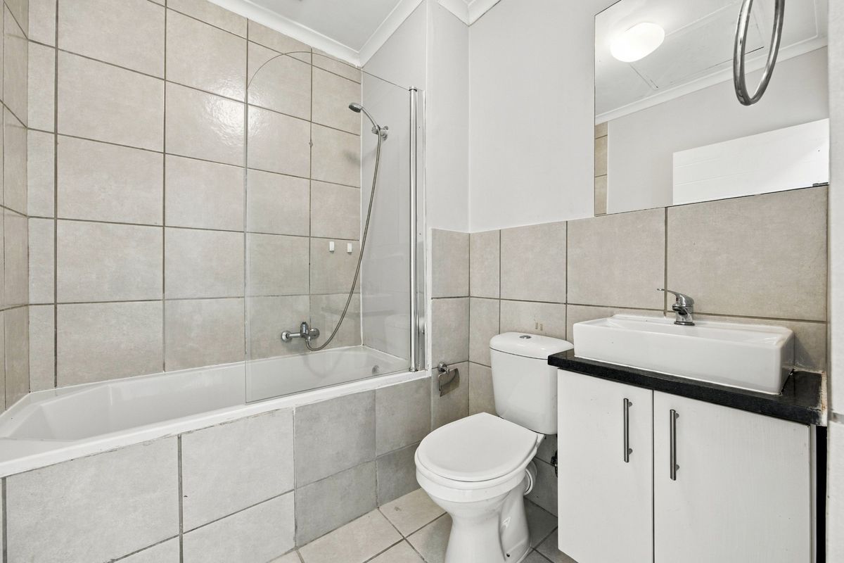 A clean, functional bathroom featuring a bathtub with a glass screen, a vanity unit with a basin, and neutral wall tiling.