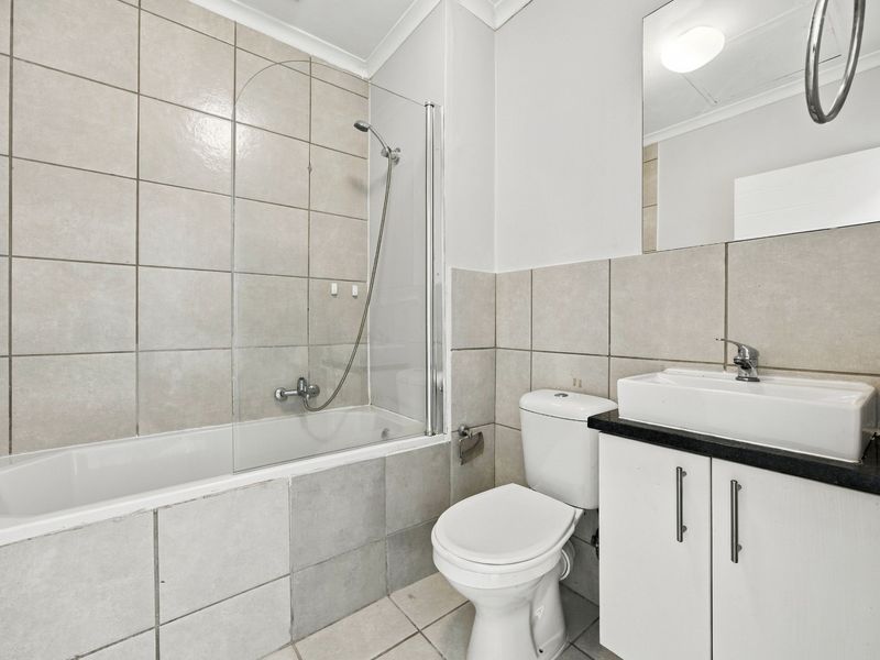 A clean, functional bathroom featuring a bathtub with a glass screen, a vanity unit with a basin, and neutral wall tiling.