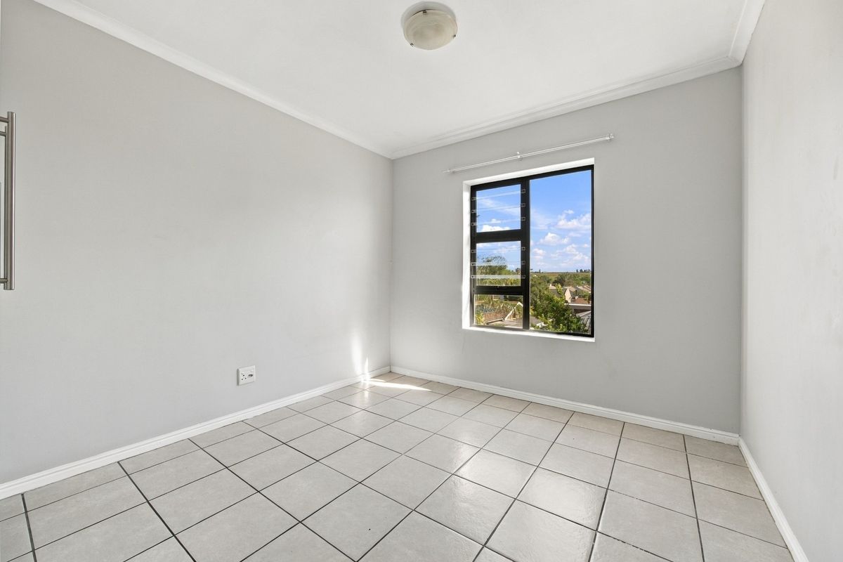 A bright, empty bedroom featuring neutral tiled flooring, clean walls, and an aluminium-framed window with a pleasant exterior view.