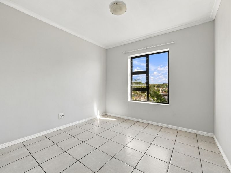 A bright, empty bedroom featuring neutral tiled flooring, clean walls, and an aluminium-framed window with a pleasant exterior view.
