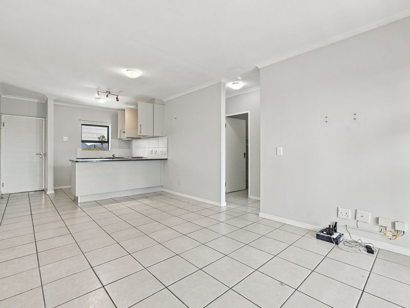 An open-plan living and kitchen area featuring tiled flooring, neutral walls, and a functional kitchen layout with built-in cabinetry and appliances.