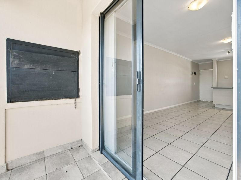 A covered balcony featuring a built-in braai and sliding glass door access to the interior living area with tiled flooring throughout.