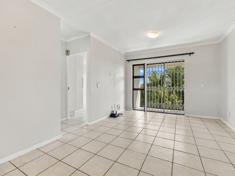 An empty, neutrally painted living room featuring tiled flooring and a sliding glass door with a security gate leading to an outdoor area.