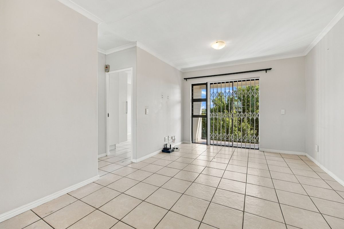 An empty, neutrally painted living room featuring tiled flooring and a sliding glass door with a security gate leading to an outdoor area.