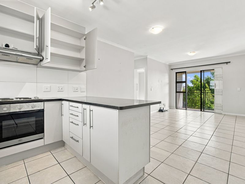 Open-plan kitchen and living area featuring tiled floors, built-in oven and hob, and a sliding door leading to a balcony.
