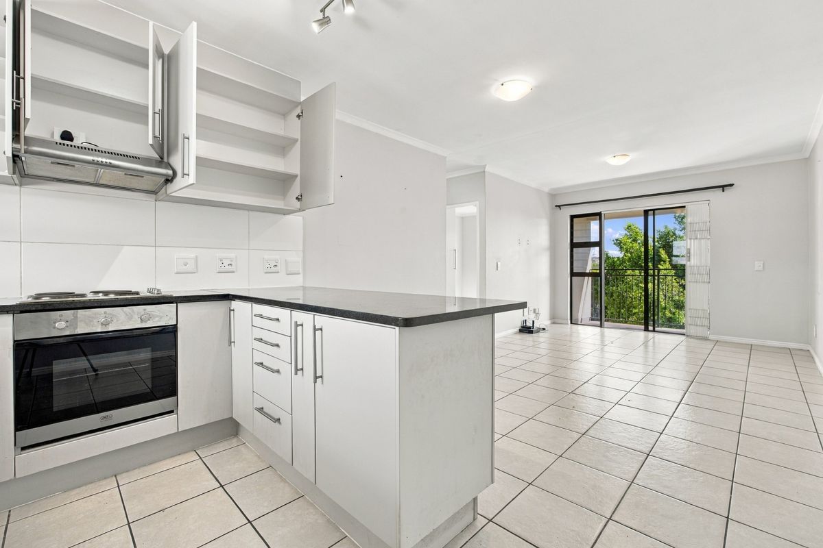 Open-plan kitchen and living area featuring tiled floors, built-in oven and hob, and a sliding door leading to a balcony.