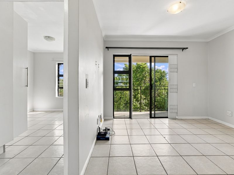 An empty, tiled living area featuring a sliding glass door that opens onto a balcony, providing natural light and outdoor access.