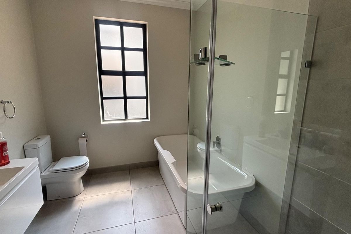 A modern, clean bathroom featuring a freestanding bathtub, a separate glass-enclosed shower, and a wall-mounted vanity unit.