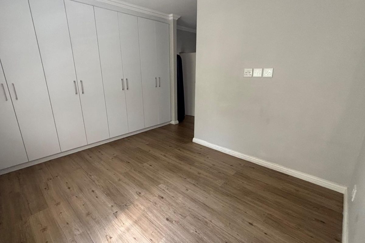 A clean, empty bedroom featuring modern laminate flooring and extensive floor-to-ceiling built-in cupboards with white cabinetry.