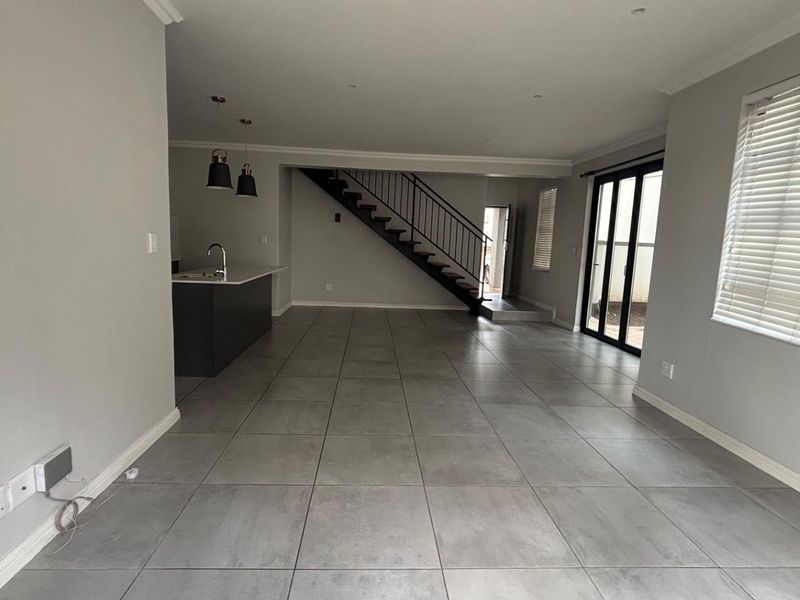 Spacious open-plan living area featuring large format floor tiles, a modern kitchen island with sink, and a staircase leading to the upper level.