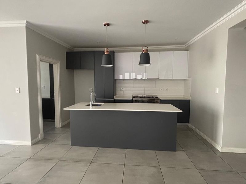 Modern kitchen featuring a central island, built-in gas hob, oven, extractor fan, and sleek two-tone cabinetry with tiled flooring.