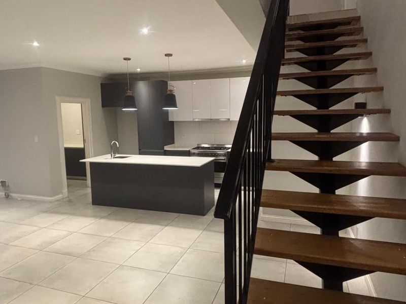 Open plan living area featuring a modern kitchen with island, sleek cabinetry, and a striking staircase with metal balustrade and timber treads.