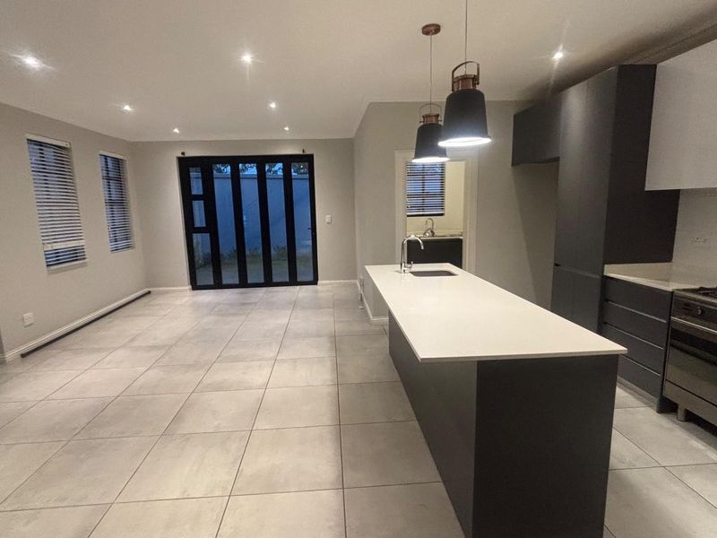 Modern open-plan living and kitchen area featuring a central island, high-end gas stove, sleek cabinetry, and large stacker doors leading to the exterior.