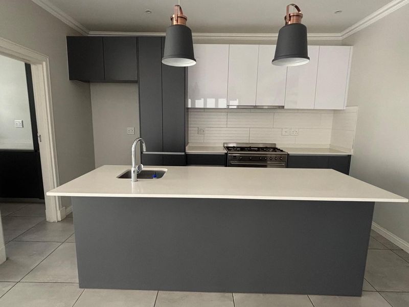 Modern kitchen featuring a central island with an undermount sink, quartz countertops, two-tone cabinetry, and a built-in gas stove with an extractor fan.
