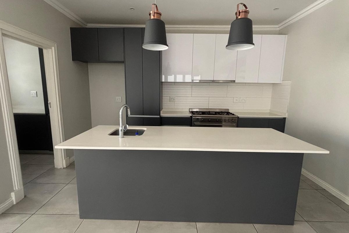 Modern kitchen featuring a central island with an undermount sink, quartz countertops, two-tone cabinetry, and a built-in gas stove with an extractor fan.