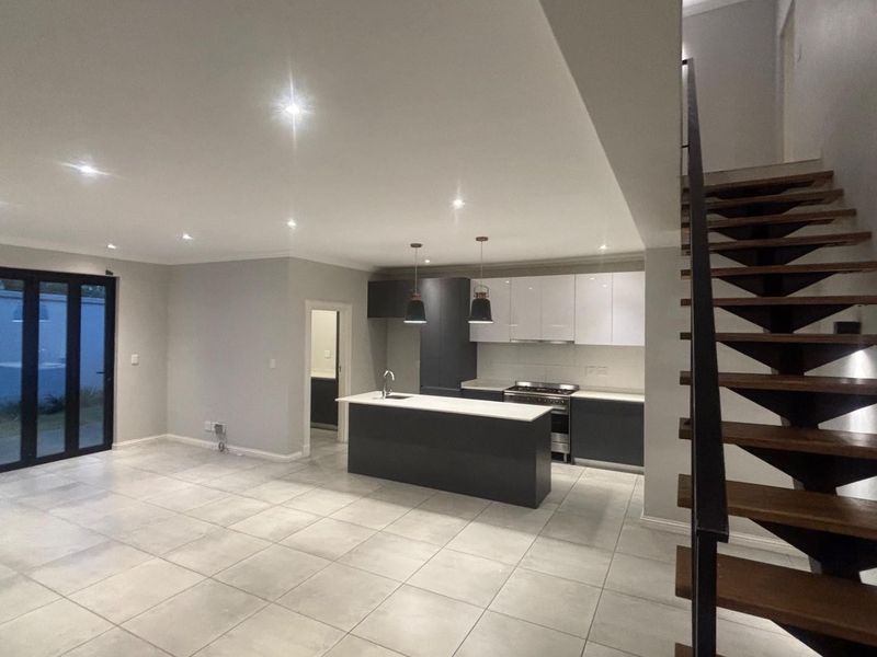 Modern open-plan living area featuring a sleek kitchen with island, tiled floors, and a contemporary staircase leading to the upper level.