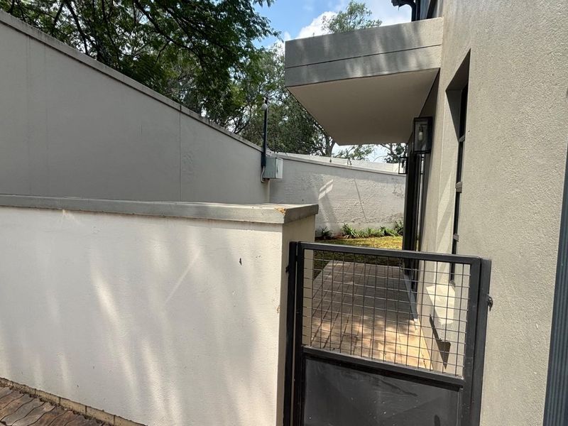 A side access path featuring a paved walkway, metal security gate, and high boundary walls, providing secure access to the rear of the townhouse.