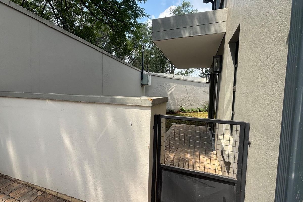 A side access path featuring a paved walkway, metal security gate, and high boundary walls, providing secure access to the rear of the townhouse.