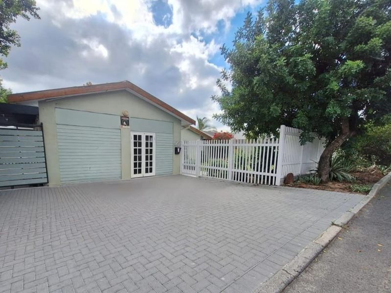 Front exterior view of the property featuring a paved driveway, white picket fencing, and a garage entrance with double glass panel doors.