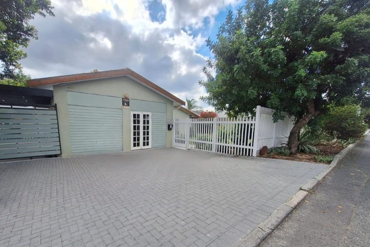 Front exterior view of the property featuring a paved driveway, white picket fencing, and a garage entrance with double glass panel doors.