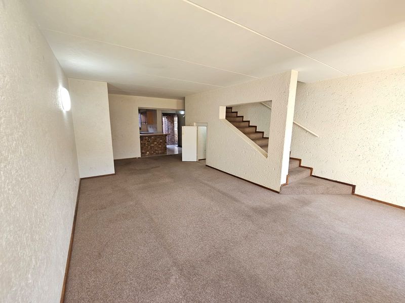 Spacious, empty living area featuring a central staircase with a cut-out wall detail, leading through to a kitchen area.