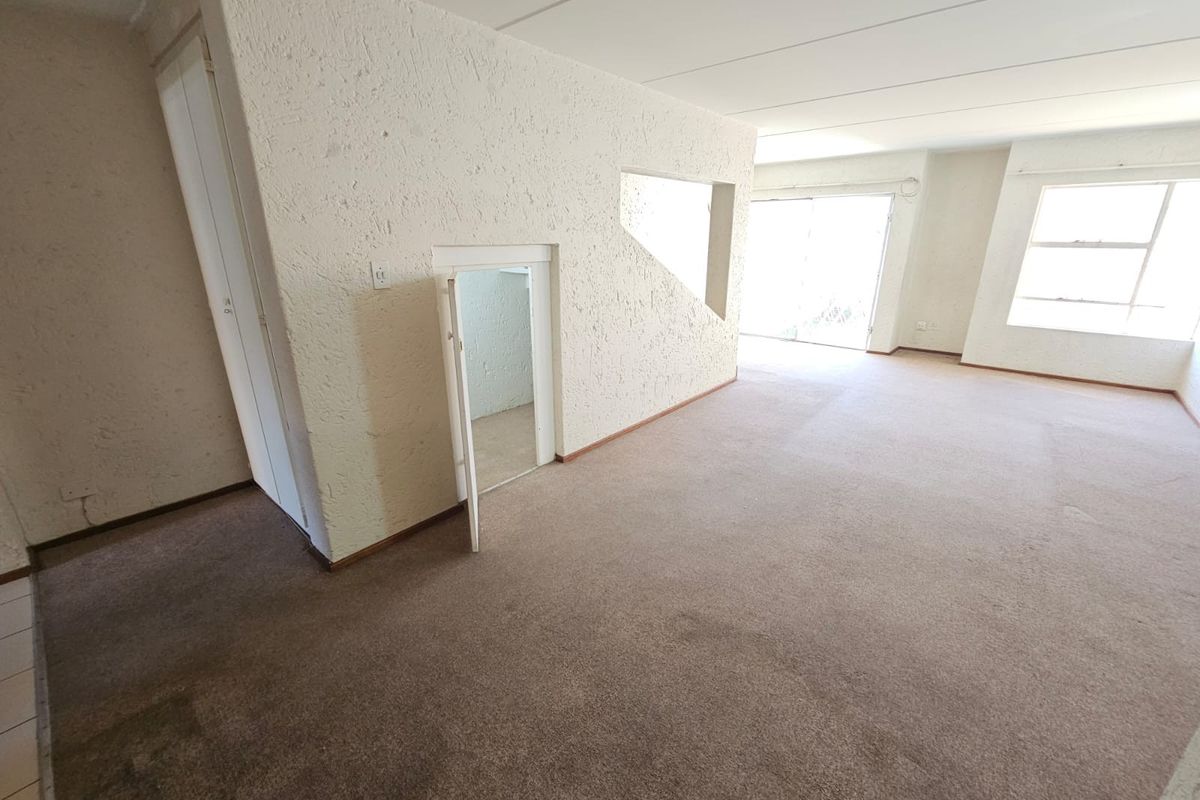 Spacious, empty living area featuring textured walls, carpeted flooring, and a unique under-stair storage cupboard, leading out to a bright patio area.