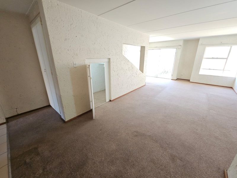 Spacious, empty living area featuring textured walls, carpeted flooring, and a unique under-stair storage cupboard, leading out to a bright patio area.