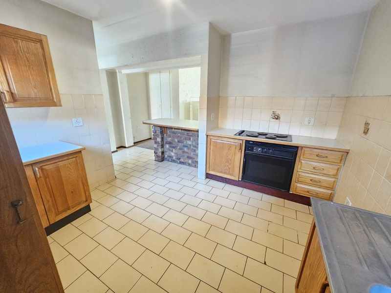 A dated kitchen featuring wooden cabinetry, built-in oven and hob, tiled splashbacks, and a breakfast bar with a brick base.