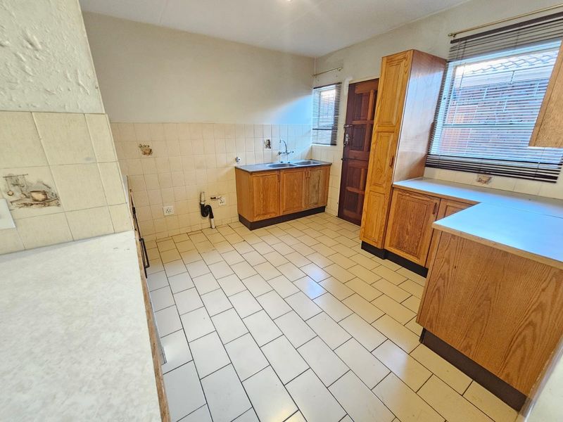 A functional, empty kitchen featuring wooden cabinetry, double sink, tiled splashbacks, and tiled flooring, offering a blank canvas for modern renovation.