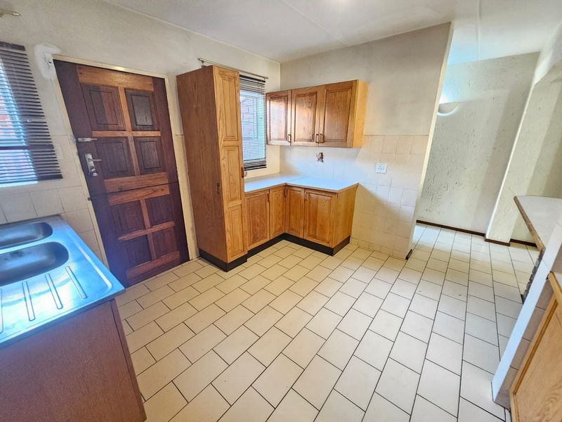 A functional kitchen space featuring built-in wooden cabinetry, a double stainless steel sink, and tiled flooring, offering a blank canvas for renovation.