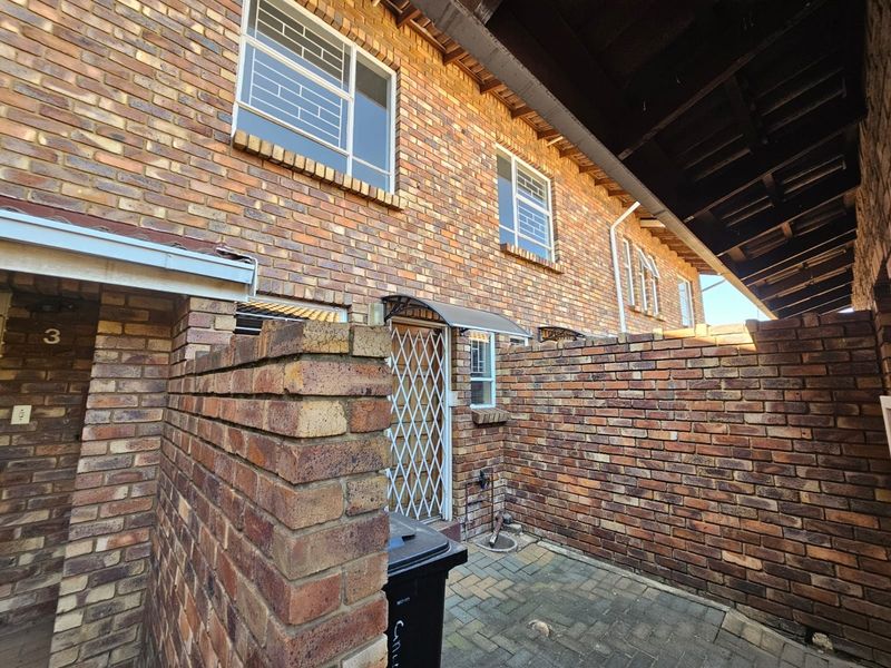 Front exterior view of a townhouse featuring face brick construction, a paved entrance courtyard, and security fixtures on windows and doors.